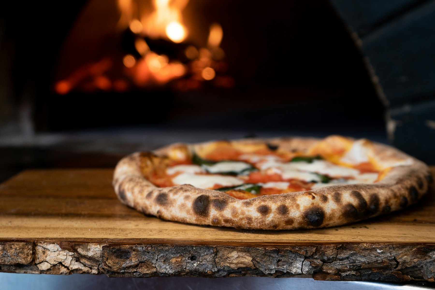 A pizza coming out of the woodfired oven